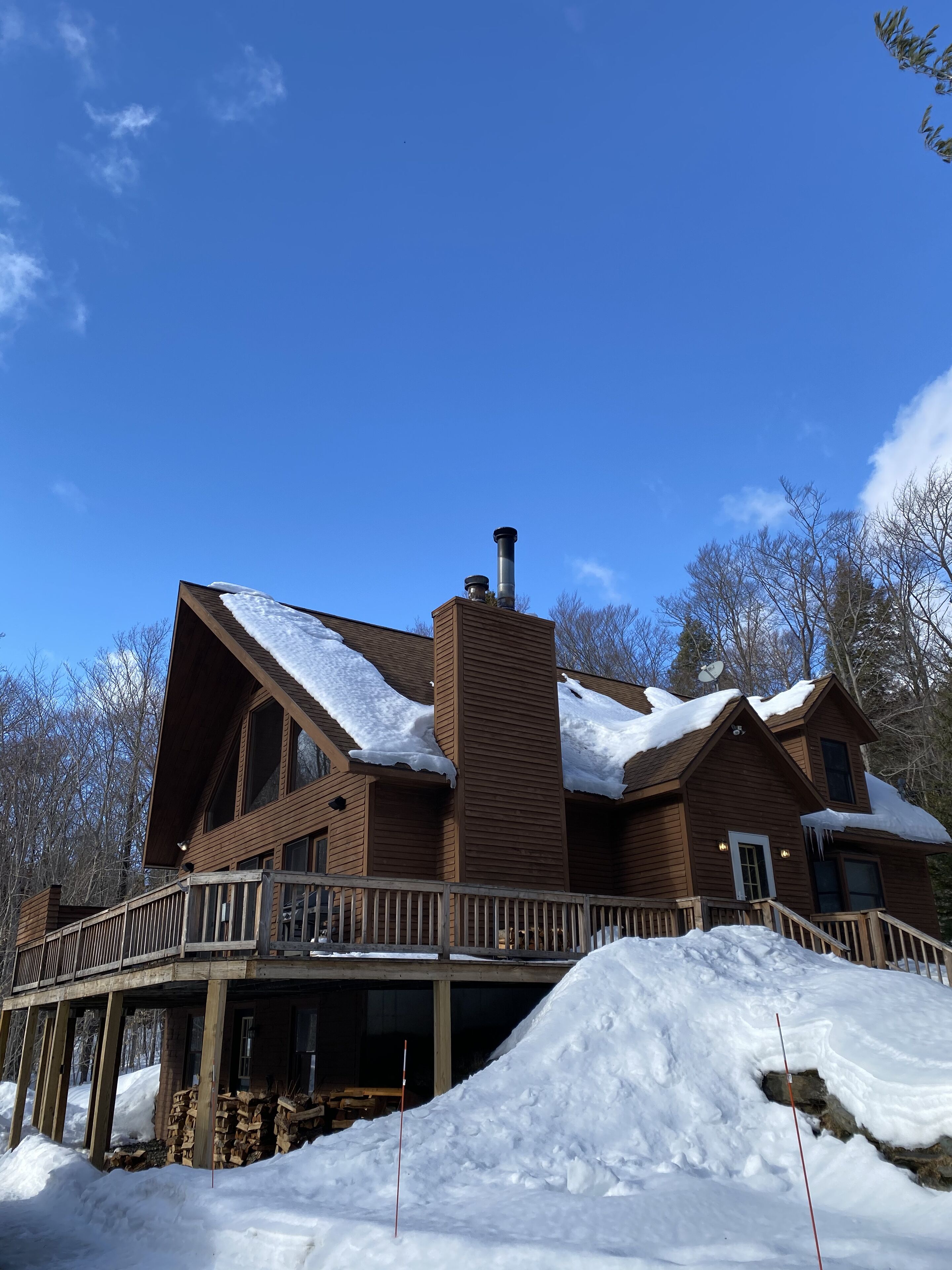 A large wooden cabin with a chimney, a deck, and snow accumulation around the property.