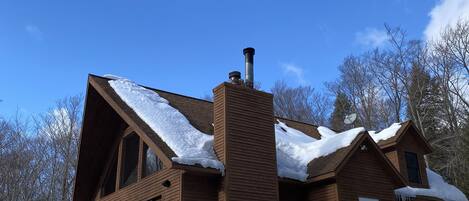 A large wooden cabin with a chimney, a deck, and snow accumulation around the property.