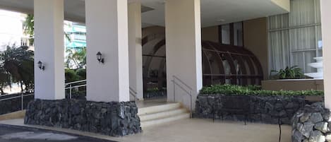 Entrada de hotel con un corredor cubierto, pilares de piedra y una escalera que conduce al edificio.