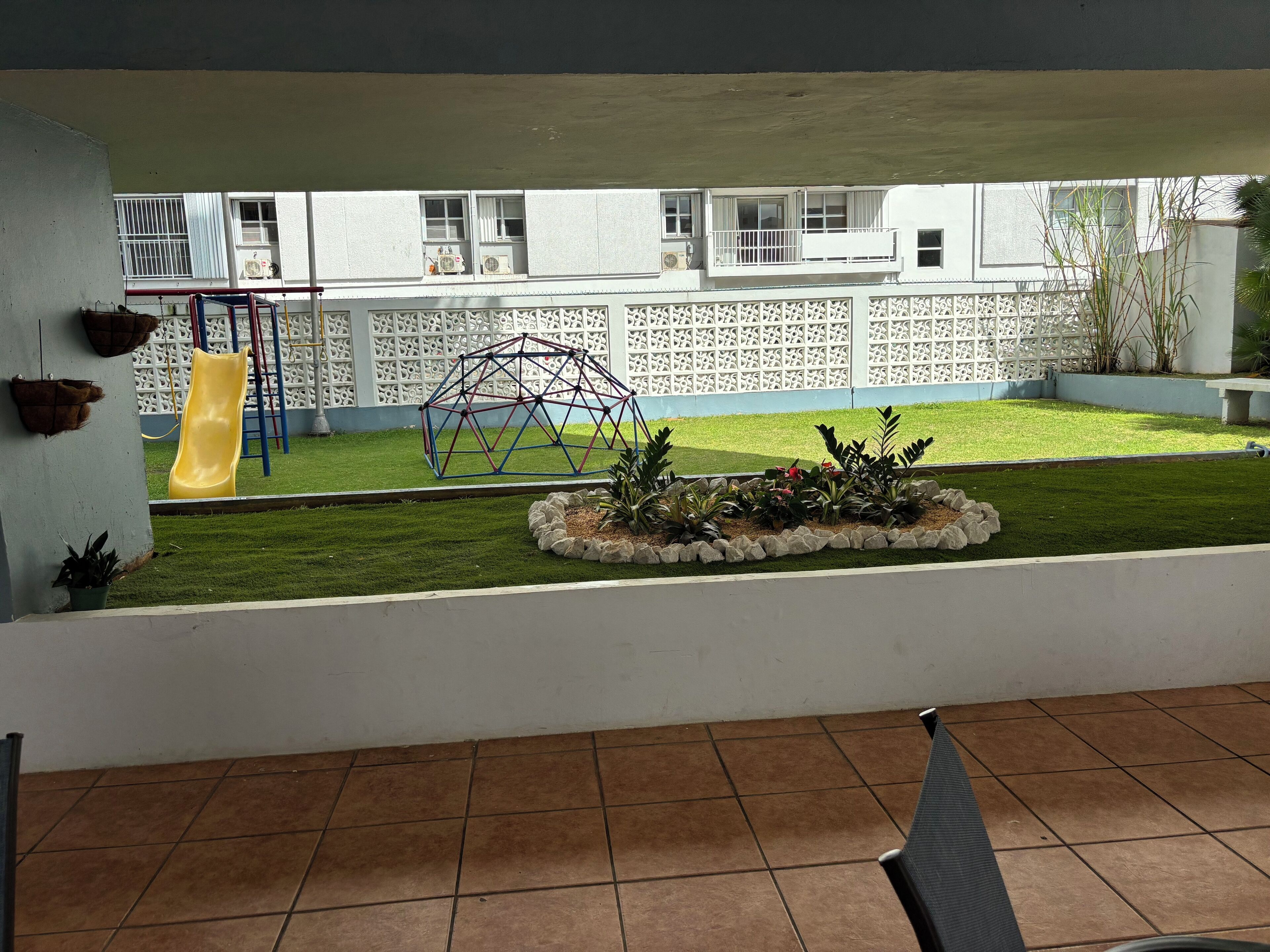 A patio with a tiled floor, a yellow slide, a swing set, and a decorative fence.