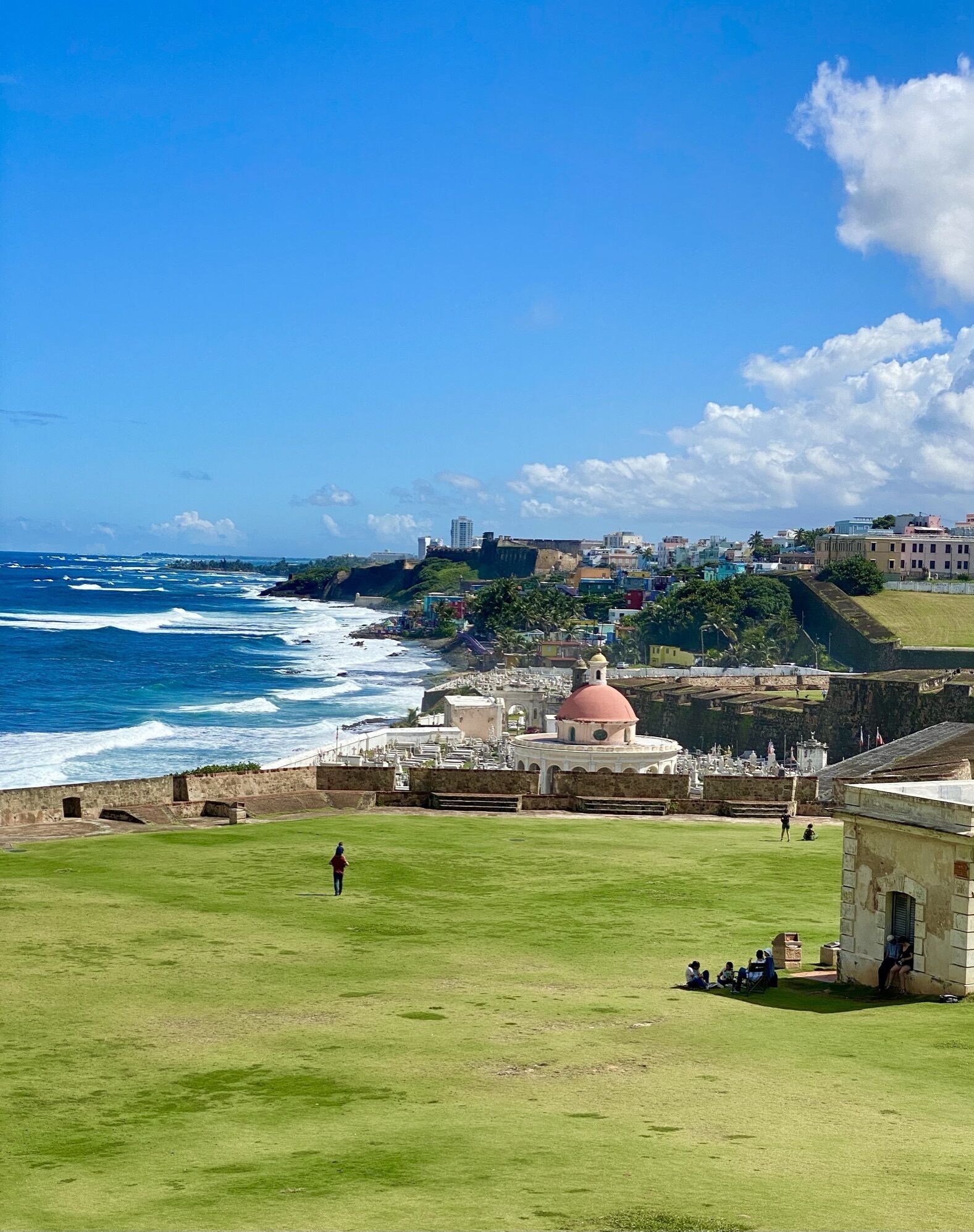 Une vue côtière avec un fort imposant et une structure en forme de dôme, des zones herbeuses et un ciel bleu dégagé.