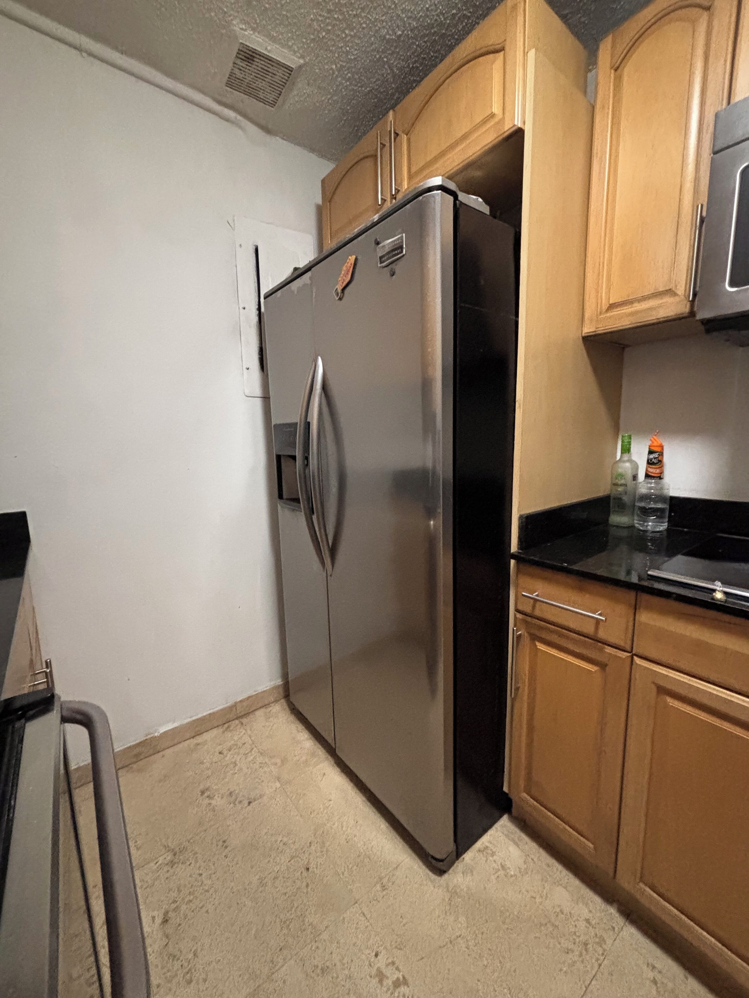 A kitchen with a stainless steel refrigerator, wooden cabinets, and a black countertop.