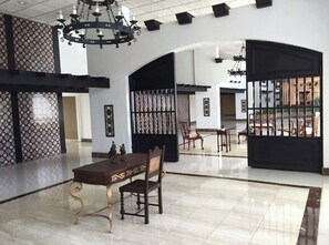 Welcome to our lobby, featuring a high ceiling, chandeliers, a reception desk, and a decorative wall with a patterned design.