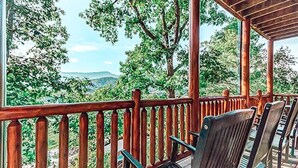 Una terraza de madera con sillas y barandilla, con vistas a un paisaje montañoso.