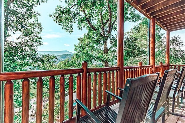A wooden deck with chairs and a railing, overlooking a mountainous landscape.