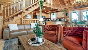 Un interior de madera con una escalera, un sofá, un sillón de terciopelo rojo y una mesa baja con controles remotos.
