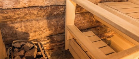 A wooden bench with a metal frame, a wooden wall, and a metal rack holding firewood.