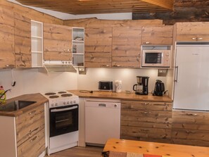 A compact kitchen with wooden cabinets, a built-in microwave, a stove, and a dishwasher. - Rukankuukkeli c 24 by Interhome (Kuusamo)