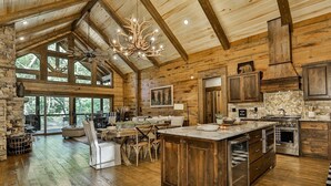 A spacious log cabin interior with a large dining area, kitchen, and a stone fireplace. - Riverscape | Ellijay, GA (Ellijay)