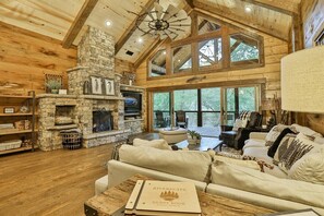 A rustic cabin interior with a stone fireplace, wooden beams, a large window, and a guest book on a table. - Riverscape | Ellijay, GA (Ellijay)