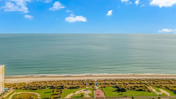 Vista sulla costa con spiaggia, oceano e un parco con un edificio a tetti rossi.