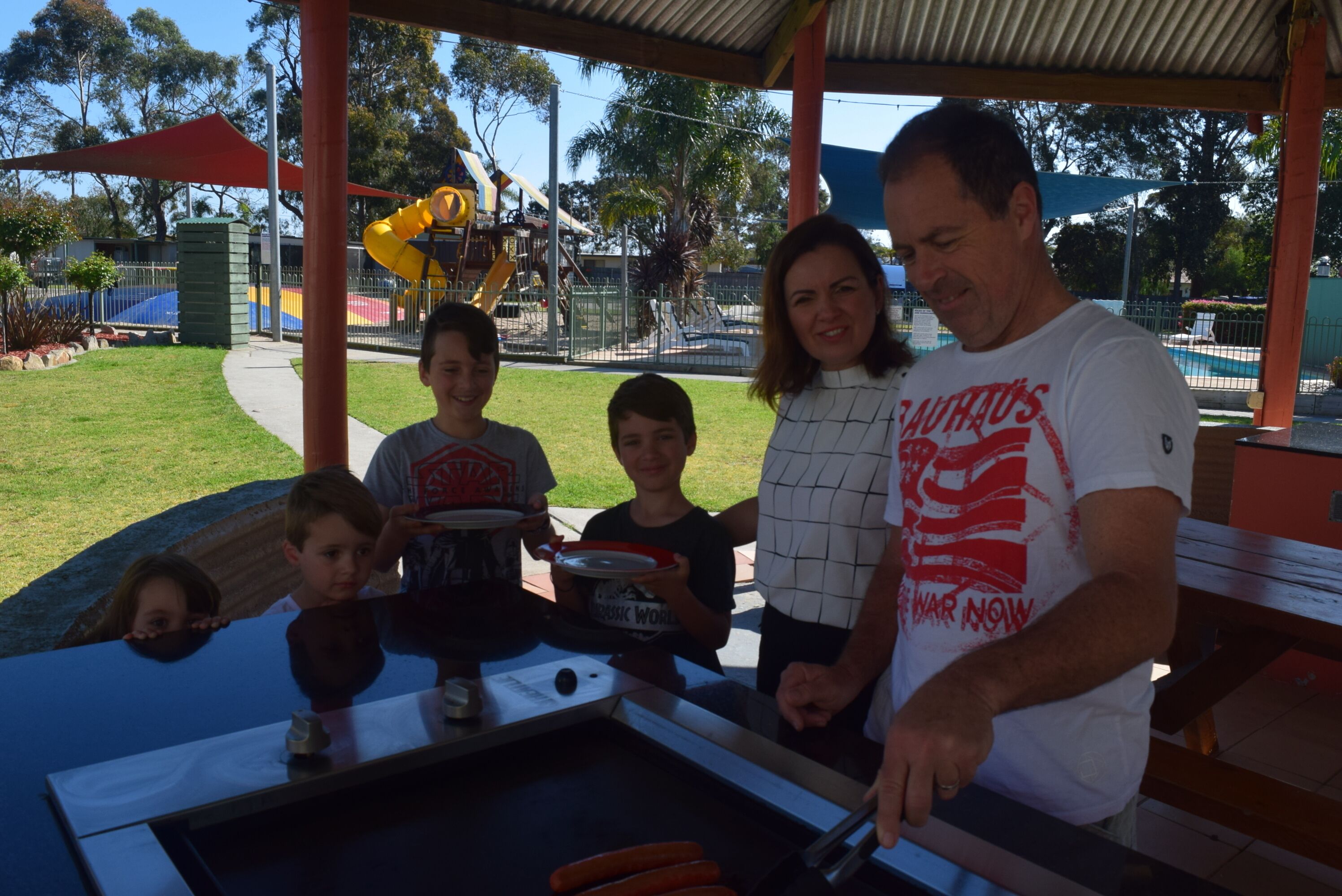 A family at a barbecue grill with a playground in the background.