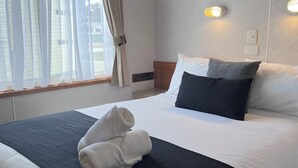 A neatly made bed with a dark headboard, white bedding, and a folded towel on the footboard. - Paynesville Holiday Park (Paynesville)