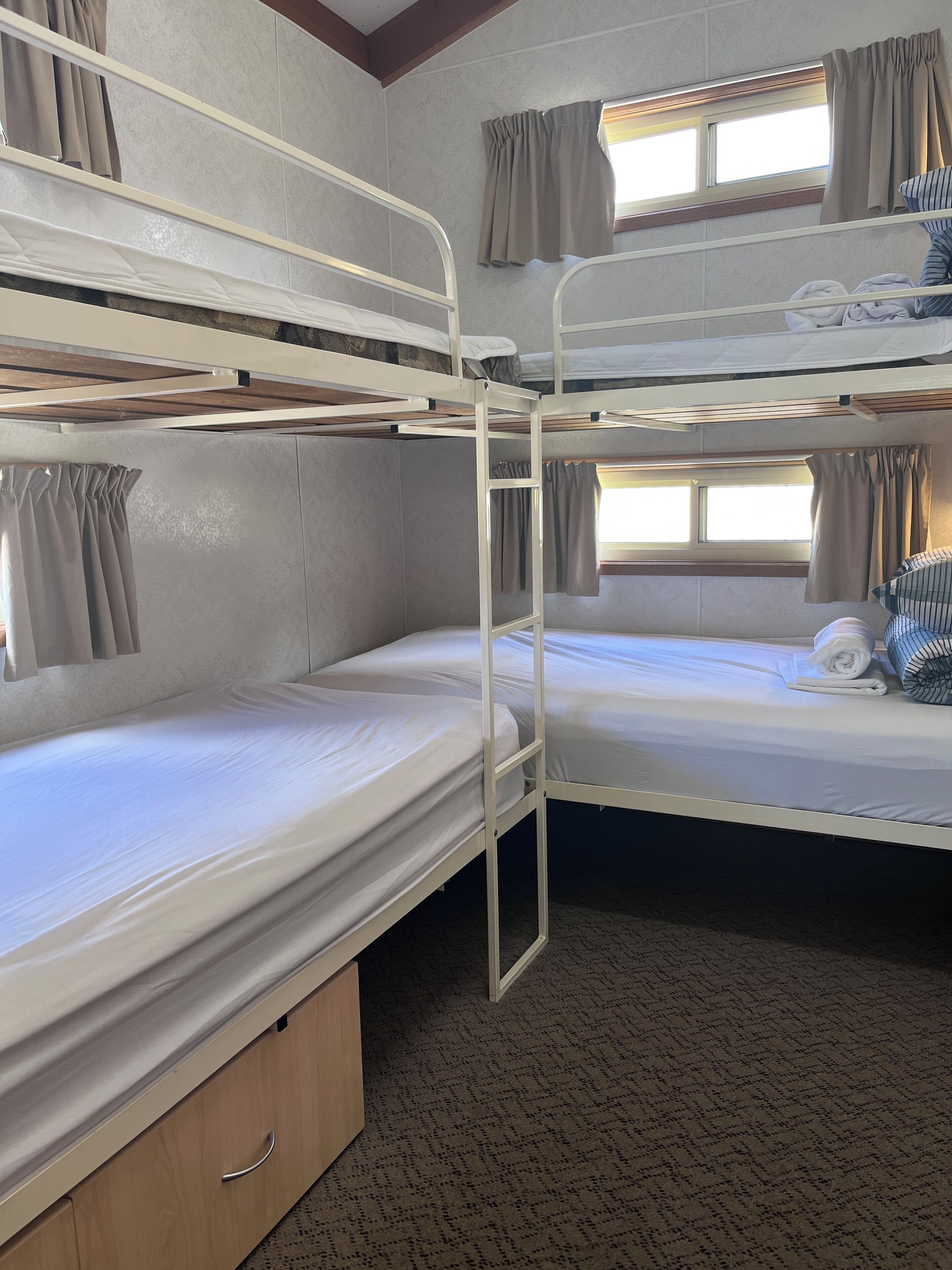 A bunk room with two beds, a wooden cabinet, and a window with curtains.