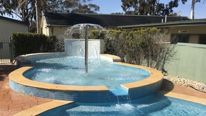 A circular pool with a central water feature and a surrounding tiled deck. - Paynesville Holiday Park (Paynesville)