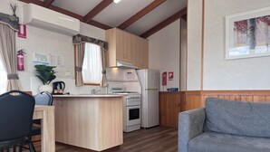A compact kitchen with a central island, a dining area with a chair, a sofa, and a coffee table with a plant. - Paynesville Holiday Park (Paynesville)