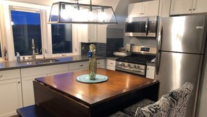 A modern kitchen with a wooden dining table, bench, stainless steel appliances, and a window overlooking the backyard. - Red Barn Retreat - Shawangunk Mountains Getaway (Gardiner)