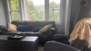 A living room with a grey sofa set, a coffee table, and a view of greenery through large windows. - Red Barn Retreat - Shawangunk Mountains Getaway (Gardiner)