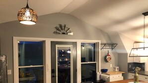 A compact kitchen with a dining area, featuring a wooden table, two barstools, and a hanging light fixture. - Red Barn Retreat - Shawangunk Mountains Getaway (Gardiner)