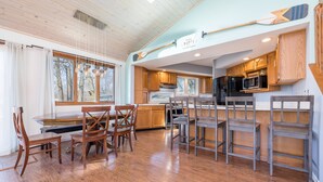 A spacious kitchen with wooden cabinets, a dining area with a table and chairs, and a view of trees through large windows.