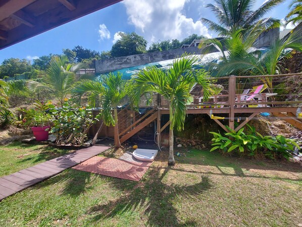A wooden deck with colorful chairs, a small palm tree, and a concrete wall in a garden setting.