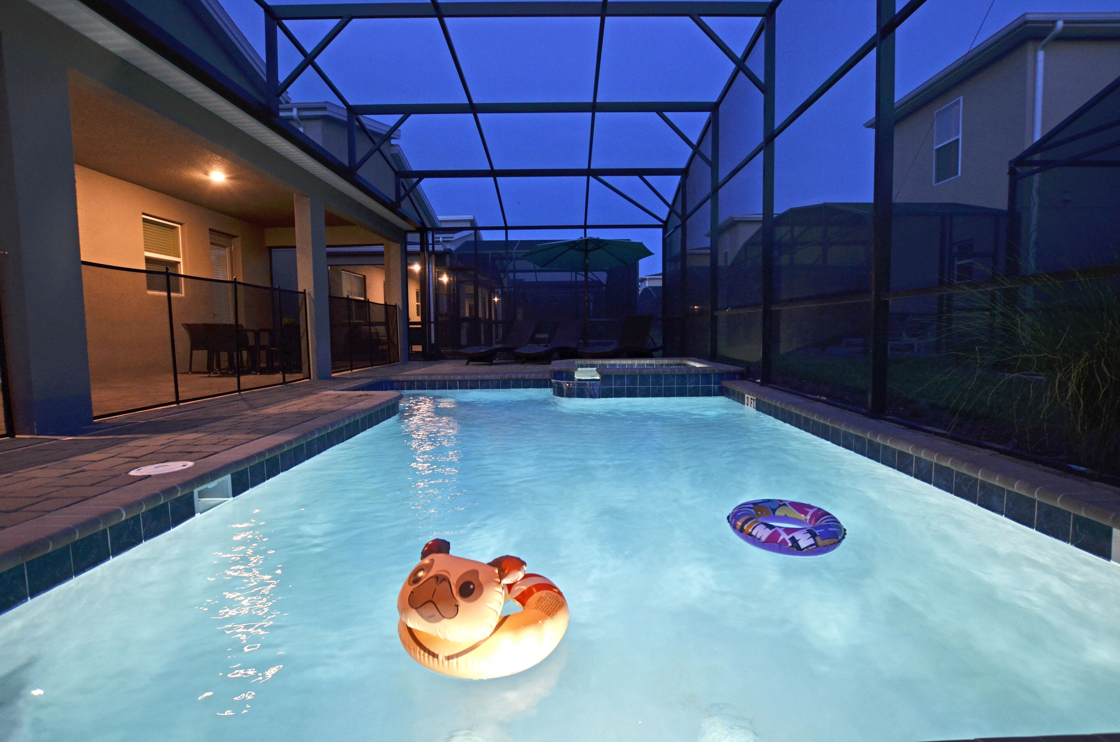 Una piscina interior con techo de cristal, zona de descanso con sillas y vista a una casa desde la piscina.
