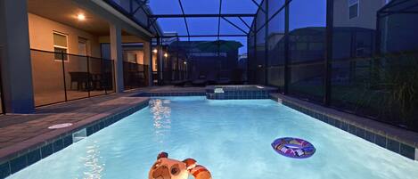 Una piscina interior con techo de cristal, zona de descanso con sillas y vista a una casa desde la piscina.