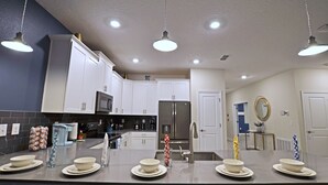 A modern kitchen with white cabinets, stainless steel appliances, and a central island with bowls and plates. - 9 BR/5 BA Resort Villa in Storey Lake Closed to Disney  (Kissimmee)
