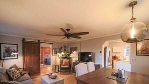 A cozy living room with a ceiling fan, a dining table, and a kitchen area in the background.