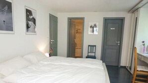 Een slaapkamer met een groot bed, een bureau met een stoel en een deur naar een andere kamer.
