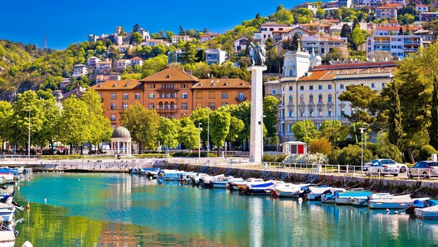 A marina with boats docked, a statue, and buildings in the background.
