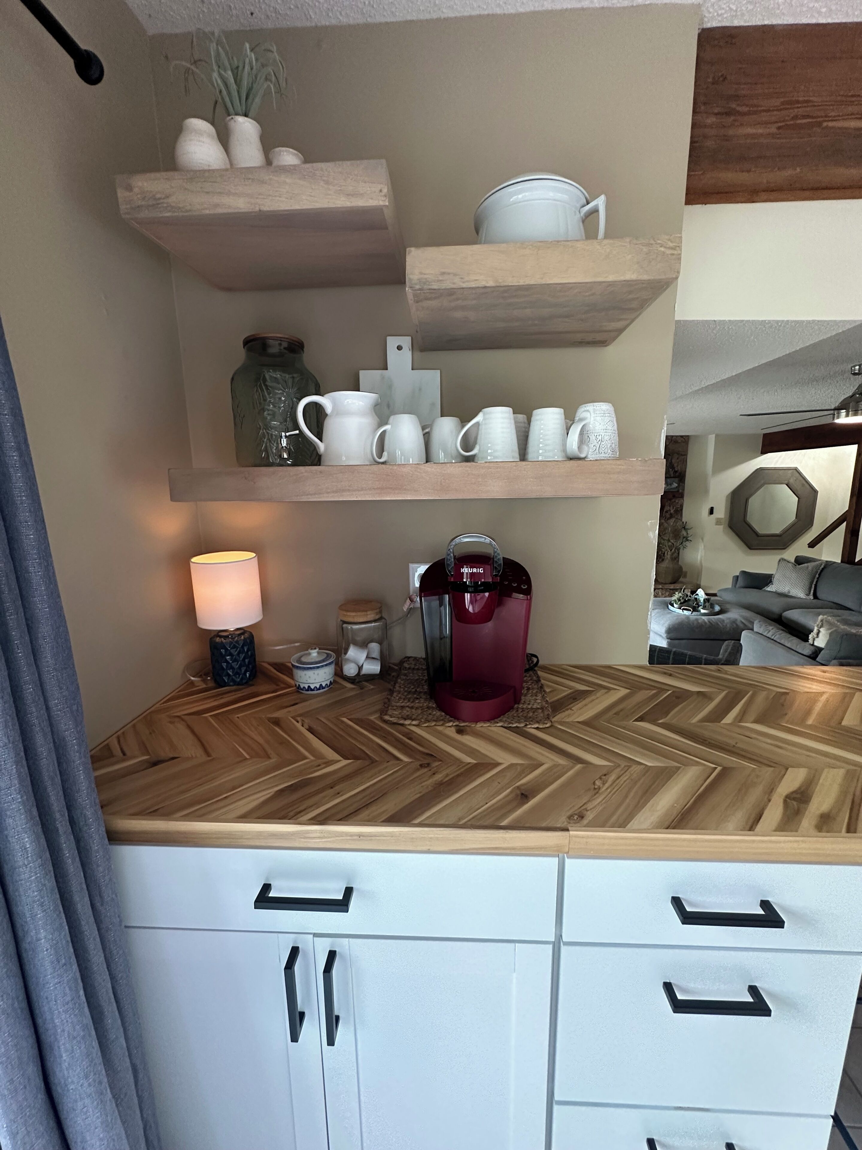 A kitchen with wooden countertops, white cabinets, a coffee maker, and decorative items on shelves.