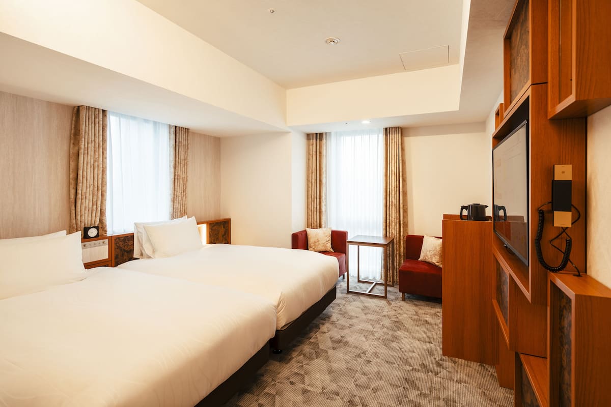 A hotel room with two large beds, a small table, a TV, and a red armchair.