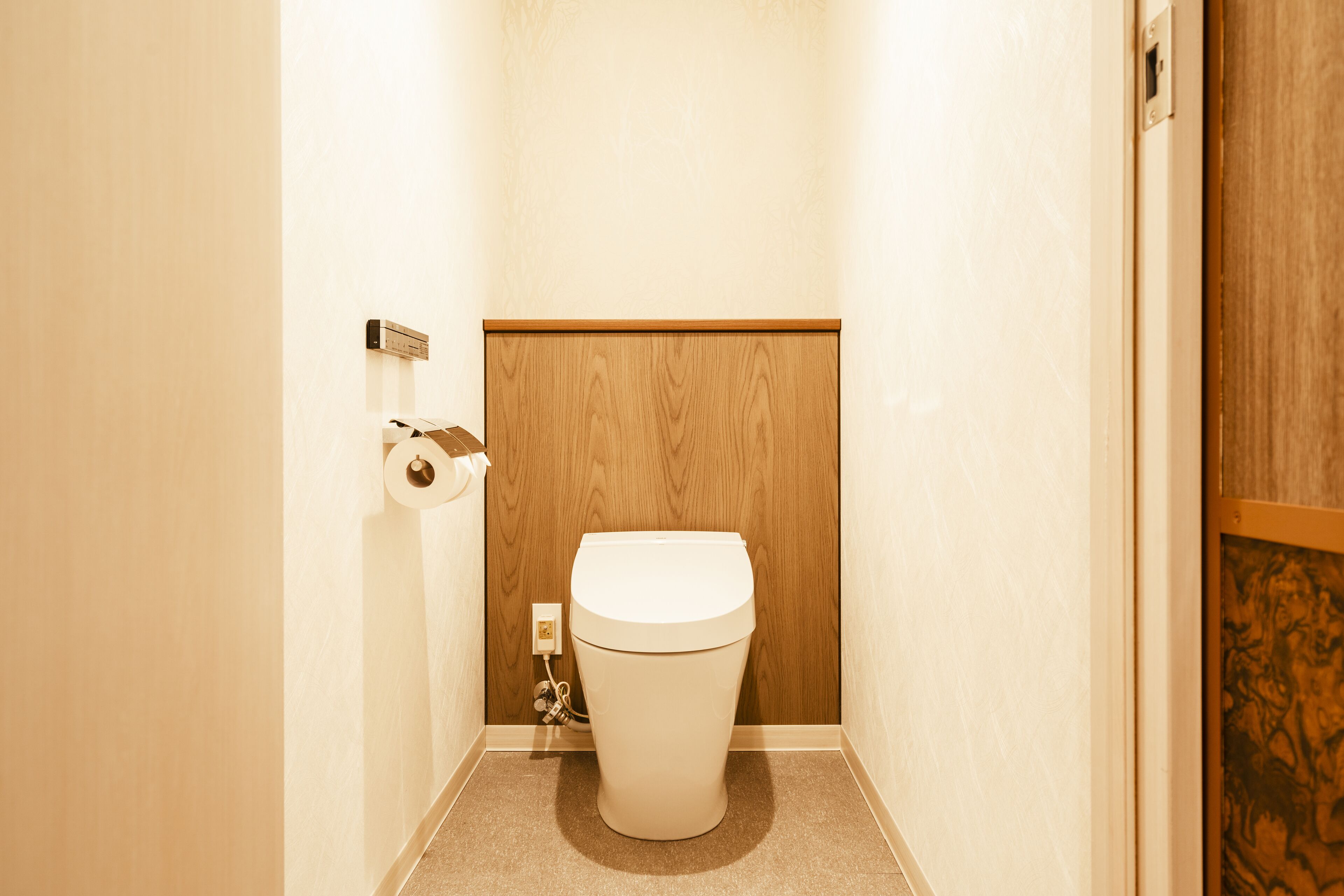 Ein kleines, kompaktes Badezimmer mit Toilette, einer Holzvertäfelung darüber und einem an der Wand befestigten Toilettenpapierhalter.