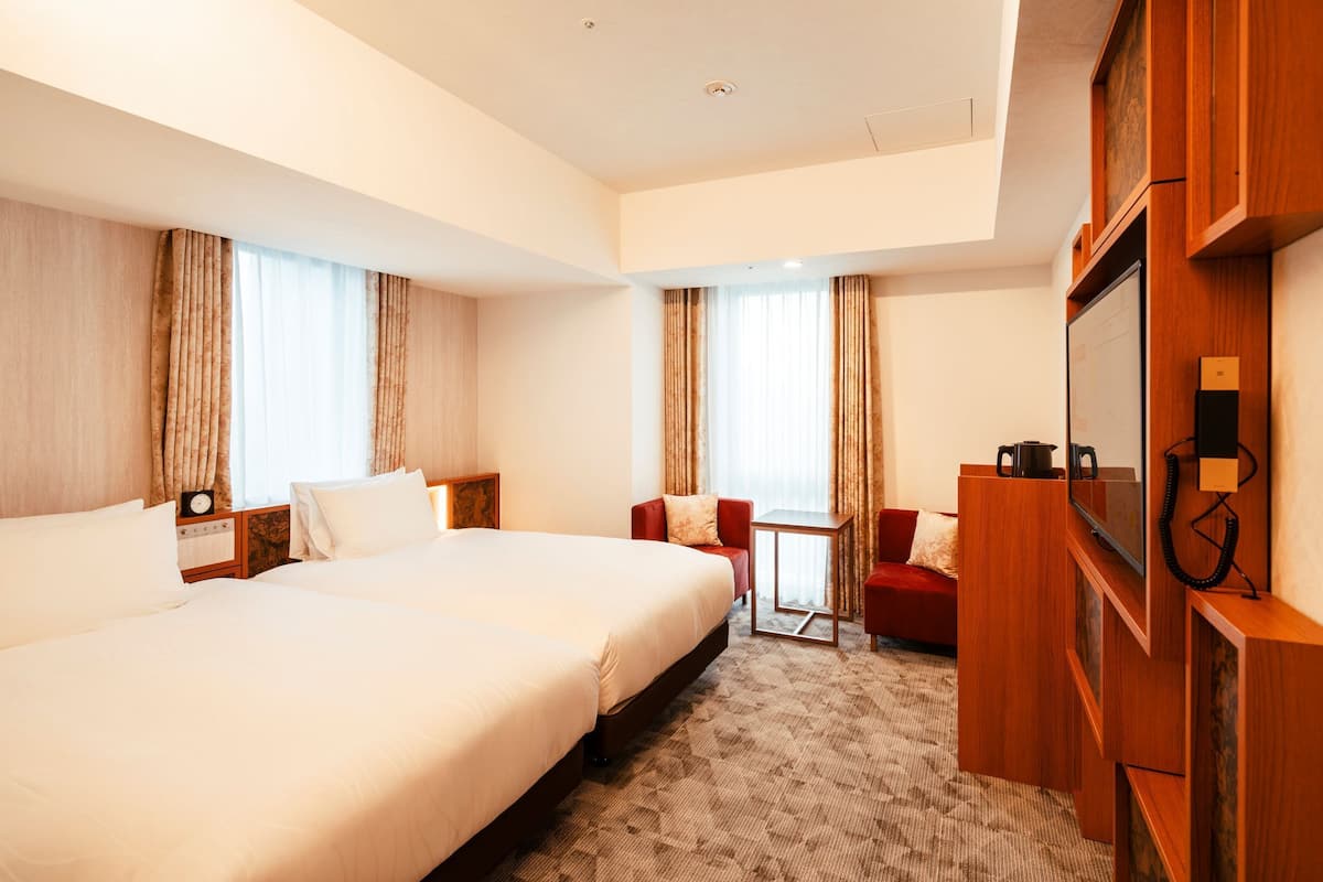 A hotel room with two beds, a TV, a desk, and a red chair.