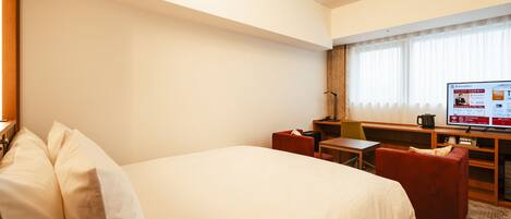 Ein Hotelzimmer mit einem großen Bett, einem Schreibtisch, einem Sessel und einem Fernseher.