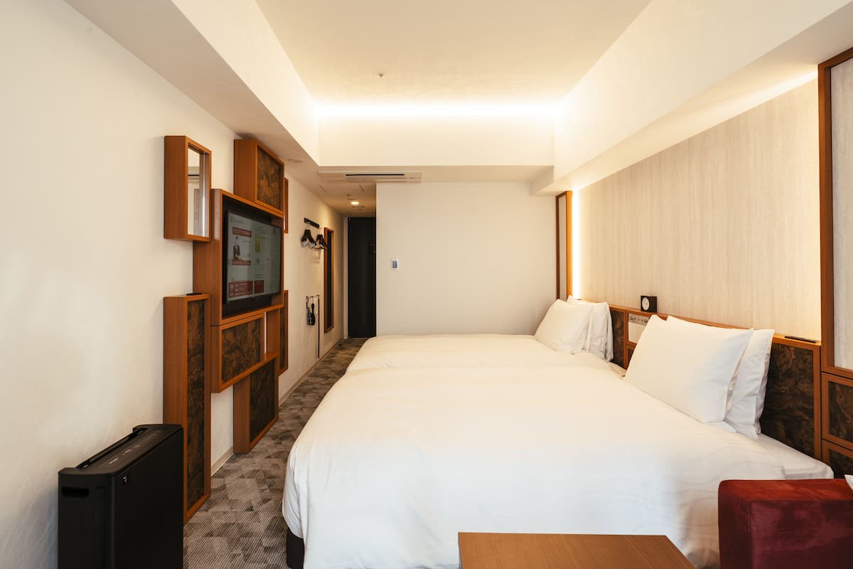 A hotel room with a large bed, a wooden headboard, a small table, and a TV on a wooden stand.