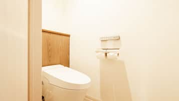 A white toilet with a wooden panel above it, a toilet paper holder on the wall, and a beige floor.