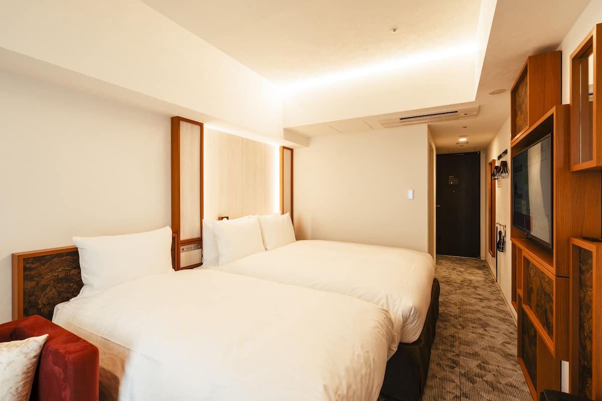 A hotel room with two beds, a TV, and a wooden wardrobe.