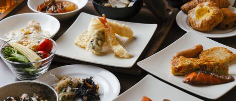Verschiedene Speisen, darunter Sushi, Tempura und Croissants, auf einem Holztisch.