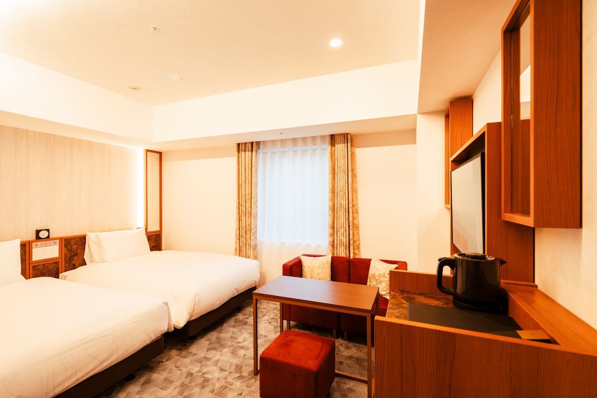 A hotel room with two beds, a small table, a sofa, a coffee maker, and a mirror.