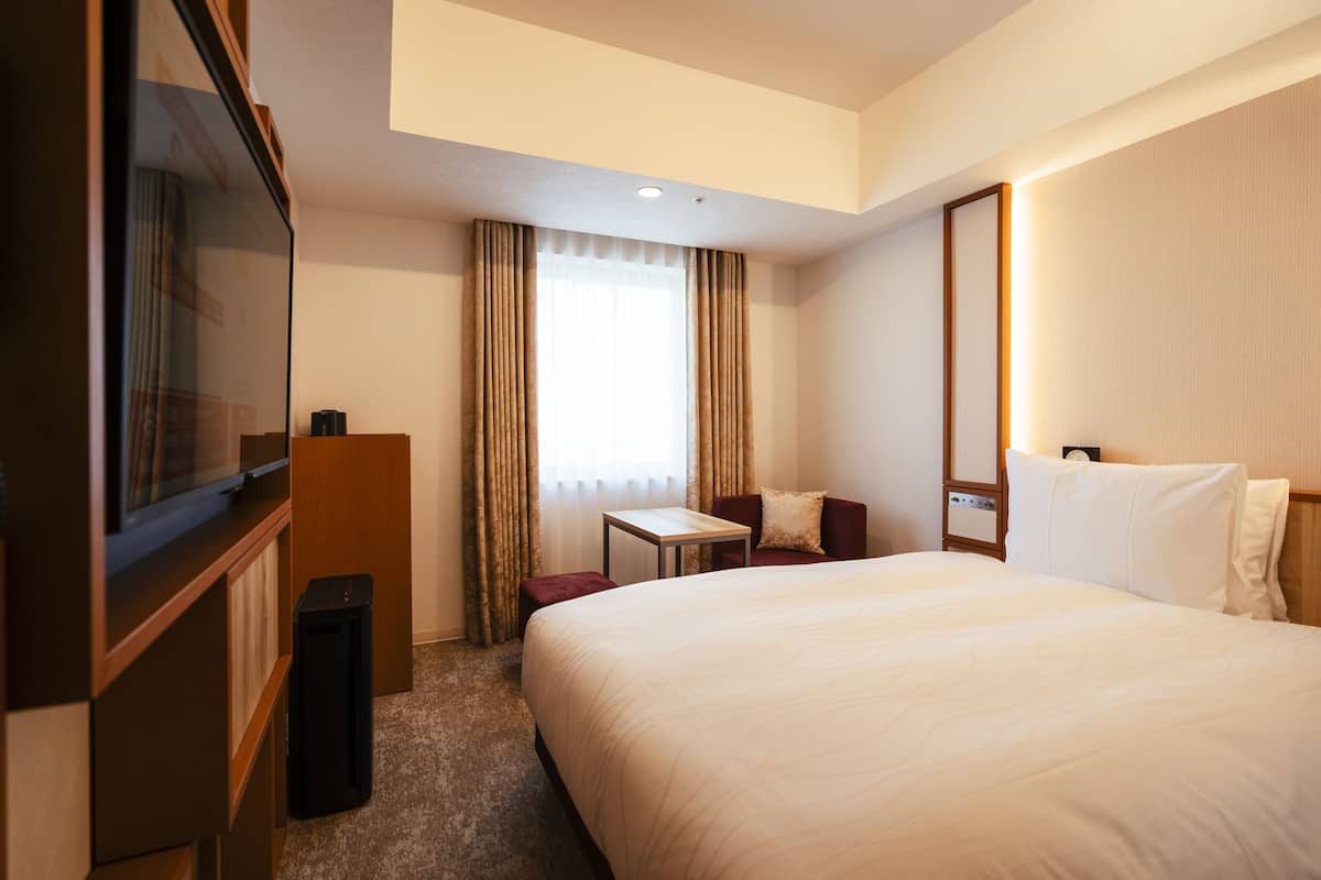 A hotel room with a large bed, a desk, a TV, and a small table.