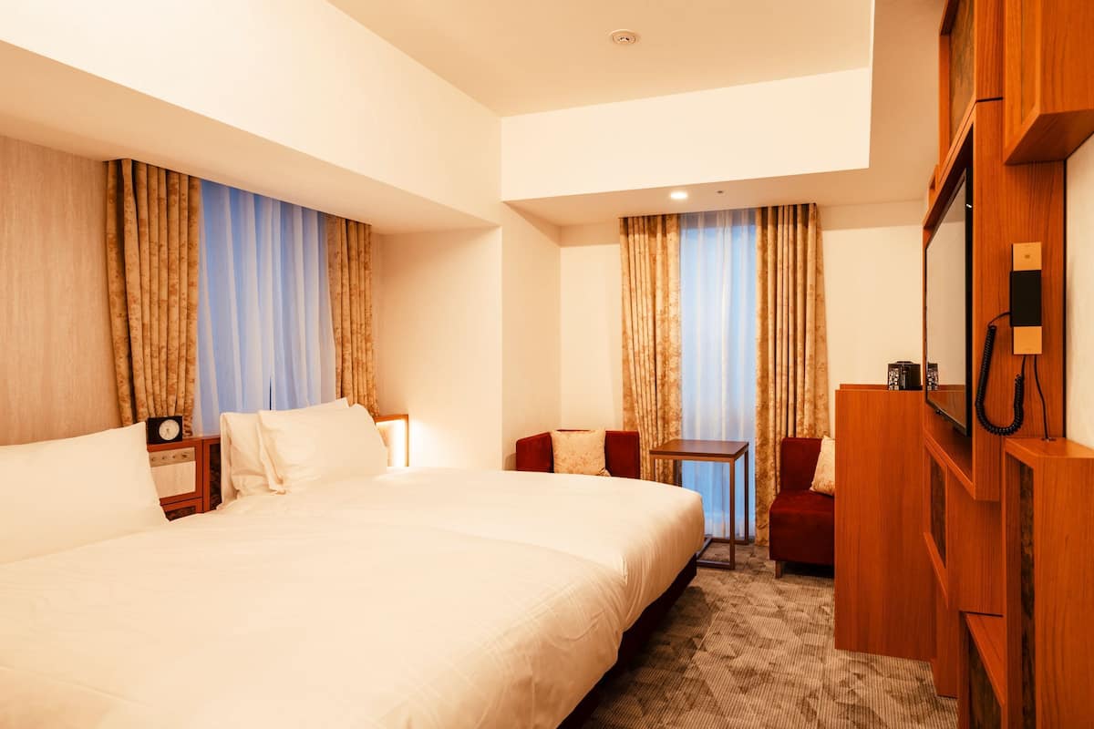 A hotel room with a large bed, a desk, a chair, a television, and curtains.