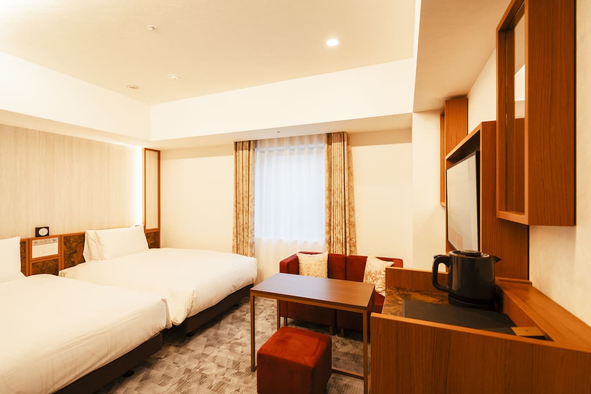 A hotel room with two beds, a small table, a coffee maker, and a mirror.