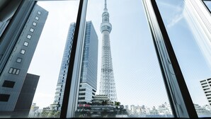 A view of the Tokyo Skytree from inside a building, with the tower's structure and surrounding high-rise buildings visible through the window.