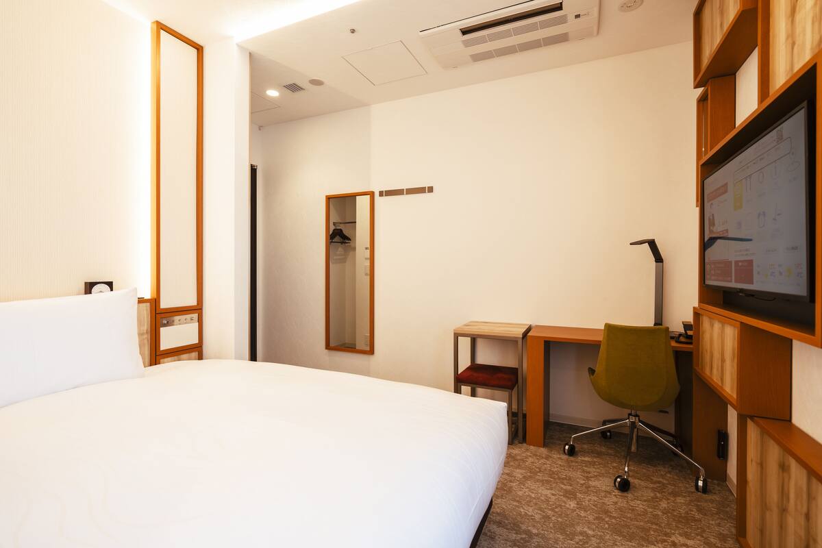 A hotel room with a large bed, a desk with a chair, a mirror, and a TV on the wall.