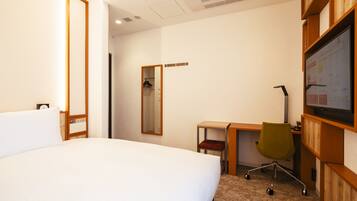 A hotel room with a large bed, a desk with a chair, a mirror, and a TV on the wall.