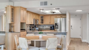 Una cocina moderna con armarios de madera, encimera de granito, refrigerador de acero inoxidable y un comedor con una mesa redonda y sillas.