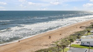 Una playa con un camino de madera, un área verde con un patio y vistas al océano.