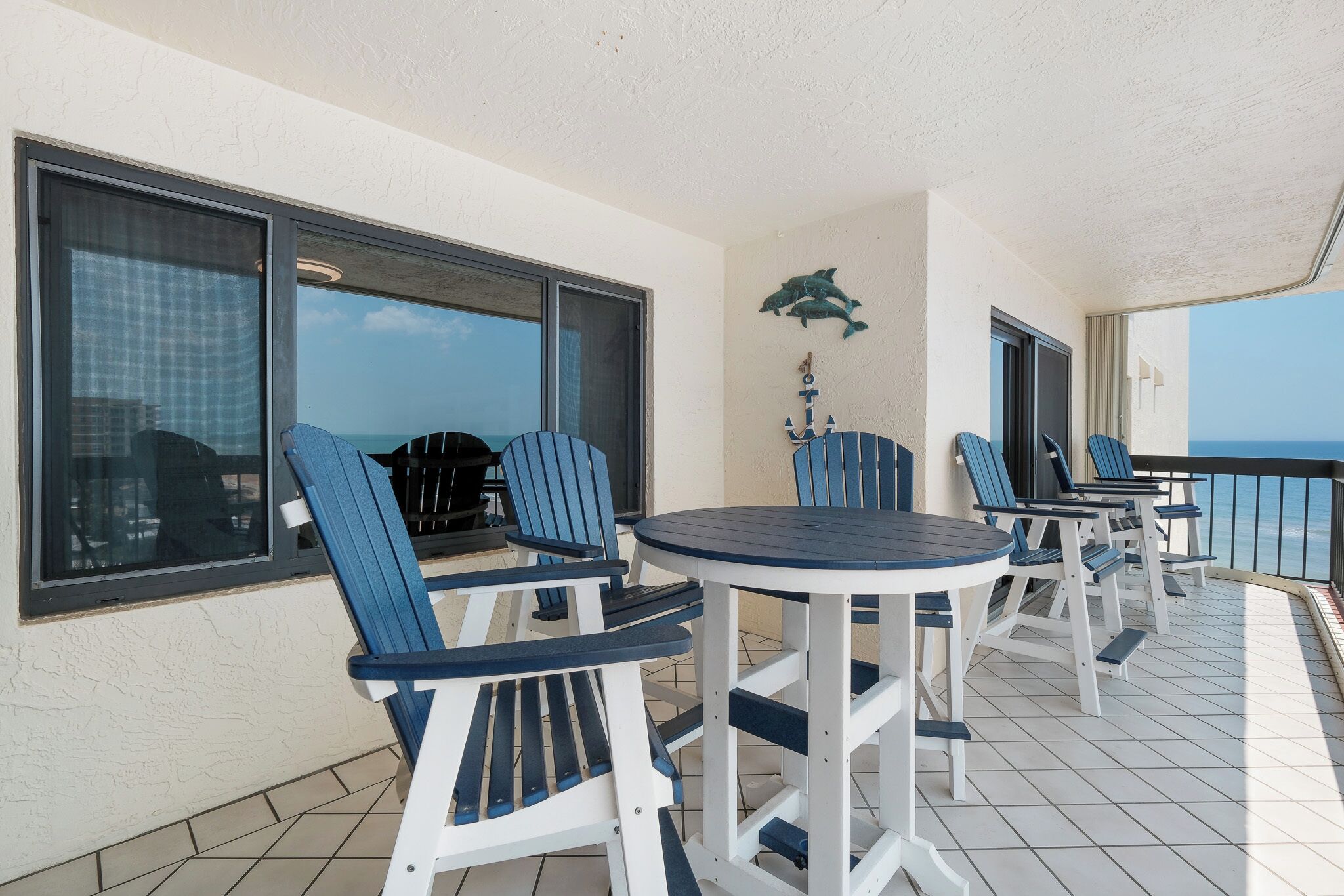 A balcony with blue Adirondack chairs and a round table, overlooking the ocean.